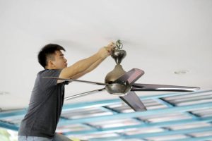 An Asian man is changing ceiling fan at residence.